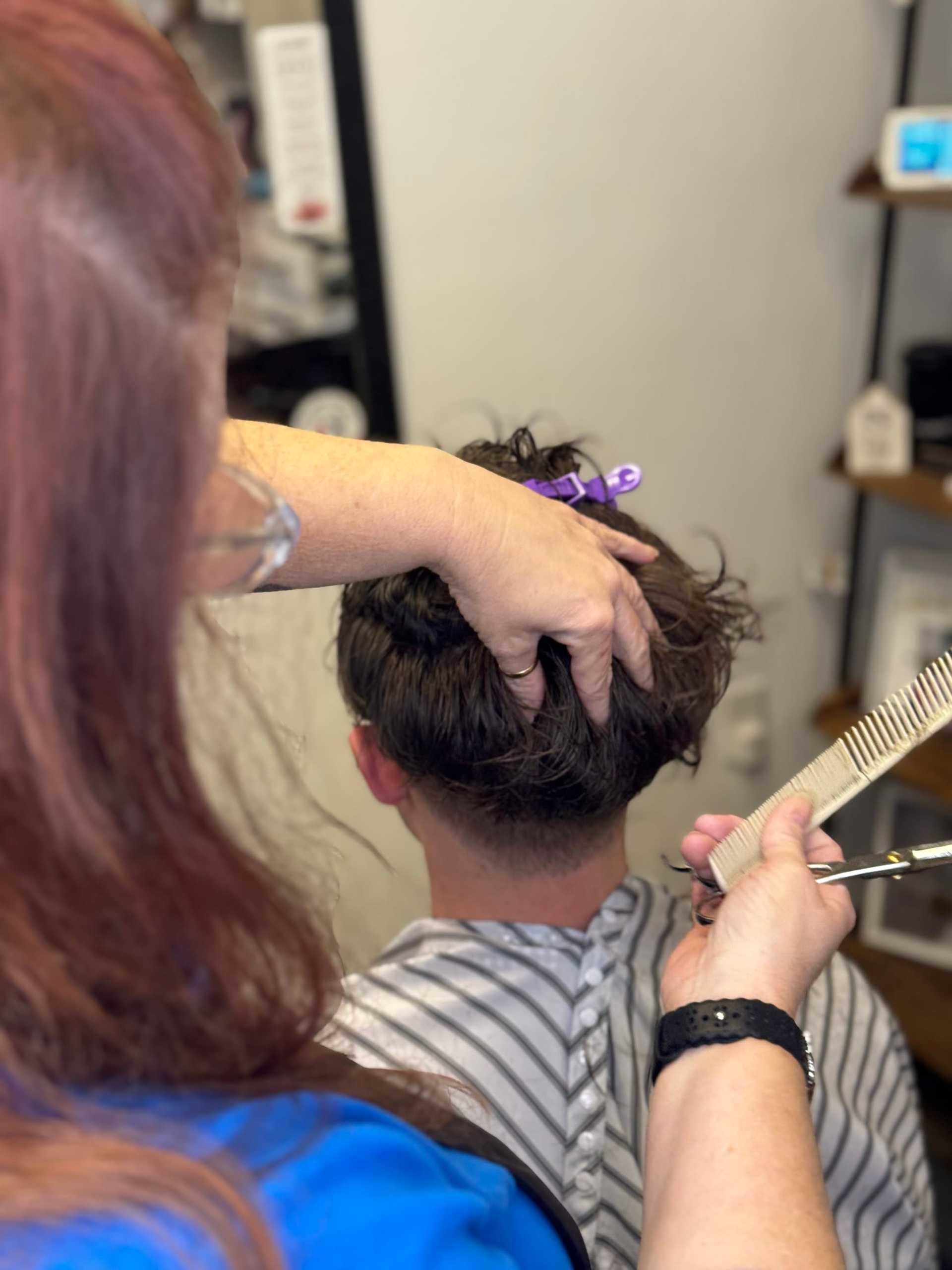 Hairdresser cutting a client's hair with scissors in a salon.
