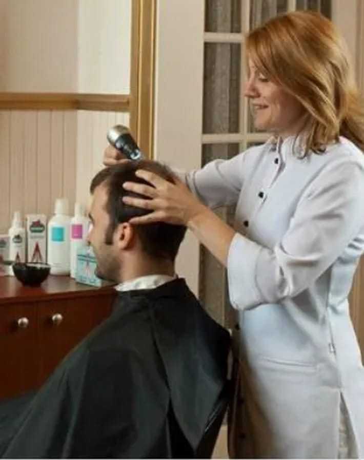 Hairdresser using a device on a seated client's scalp in a salon.